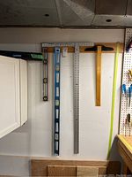 Four different types of levels hanging on a workshop wall including a wooden T-square style level, a blue metal spirit level, and a metal ruler square.