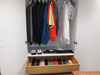 Photo of hanging jackets, white dress shirts, cargo pants, and a drawer of assorted ties. Cuff links and tuxedo accessories visible on shelf.