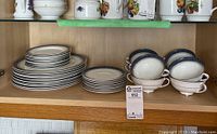 Shelf displaying stacks of plates, eight double handle cups, and saucers matching the set.