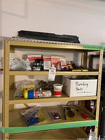 Shelf with assorted plumbing chemicals, tools, and parts including labeled box and packaged tools