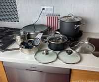 Full view of all pots, pans, lids, and thermometer arranged on kitchen counter.