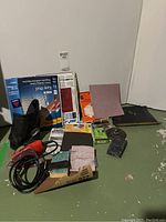 Photo of the Black & Decker Mouse electric sander with sanding pads, papers, blocks, user manual, and dust collection bag arranged on floor.