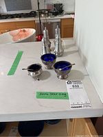 Overall view: two tall sterling shakers at rear; five salt cellars with liners and spoons at front.