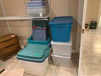 Wide view showing stacked clear plastic storage bins with blue and green lids, some smaller containers on top or beside them.