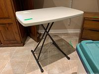 Fold up resin table with white resin top and black metal legs in extended position on tile floor.