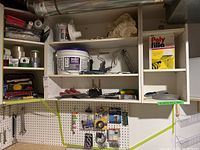 Shelf with drywall compound bucket, painting supplies, tapes and hand tools on pegboard