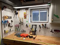 Wide view of pegboard and workbench with various tools including screwdrivers, saws, mallet, pliers, paintbrushes, toolboxes, and digital clock.