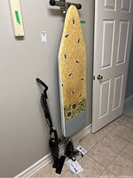 Photo showing all three items together against a wall: vacuum, ironing board with cover, and steam iron on floor.
