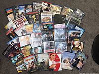 Wide shot of over 40 assorted DVD movie cases laid out on a carpeted floor, showing a variety of titles and genres.