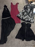 Four women's dresses laid out on carpet, including a black halter top and long skirt two-piece, burgundy sleeveless dress, black strapless floral dress, and black lace strapless dress with zipper.