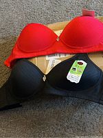 Two bras, one red and one black, displayed on a box, showing molded cups and heart charm detail.
