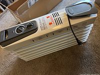 Side angle view of the light gray electric oil-filled radiator heater showing the fins and power cord wrapped around the side