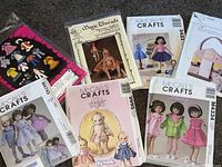 Seven sewing pattern booklets and sheets for doll clothes and accessories arranged on carpet.
