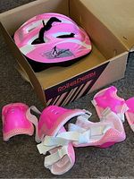 Image showing pink and white protective helmet in box alongside pink wrist guards and elbow pads with white straps
