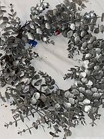 Overall view of silver metallic leaf wreath showing circular shape and dense foliage of silver leaves on brown twigs.