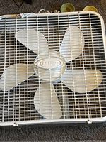 Close-up of the front view of the white Lasco box fan showing five blades and protective grille.