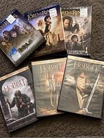 Photo showing the full set of Lord of the Rings DVD cases and Hobbit DVD cases on carpeted floor, covers clearly visible, some with stickers.