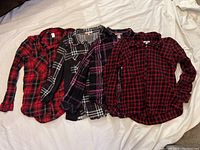 Four women's flannel button-up shirts laid out showing color and pattern variations.