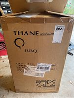 Closed cardboard box with Thane Houseware branding and BBQ label. Shipping labels and handling marks visible.
