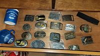 Full lot photo with all belt buckles spread out, koozie, and mug on wooden surface