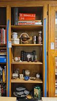 Wooden shelving unit showing all five shelves filled with books, figurines, glassware, decorative items, and other collectibles.