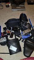 Wide view of cameras, lens, cases and accessories scattered on floor, showing multiple cameras including Kodak 8mm video camera, Sony camera with burn spot, and carrying cases.
