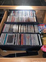 Music CDs inside a black carrying case with two compartments holding about 50 CDs total, visible artist names and album covers.