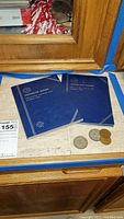 Photo showing two blue Jefferson Nickel coin books and four loose coins on a countertop.