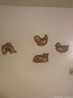 Four copper molds mounted on a wall: rooster, duck, fish, and squirrel-shaped molds