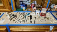 Wide view photo of a table with assorted costume jewelry items spread out including necklaces, rings, bracelets, cuff links, rosary, and tie clasp.