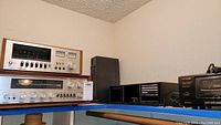 Shelf displaying vintage Pioneer stereo receiver and cassette deck with wood trim, black CD holder with CDs, and black Optimus cassette deck