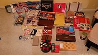 Photo showing a large assortment of classic board games, card games, poker chips, dice, and game boards arranged on floor.