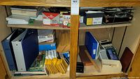 Photo showing shelves with blue 3-ring binders, calculators, packing envelopes, and a label maker.