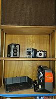 Photo of three vintage cameras on a wood shelf above the projector: Brownie Target Six-16, Kodak 8 Automatic, Kodak Brownie Holiday.