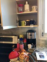 Cuisinart coffee maker, electric bean grinder, assorted mugs, decorative teapot, creamer, sugar bowl, and instruction manual on kitchen counter and cabinet shelf.