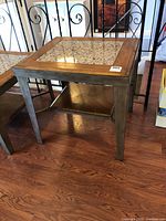 Full view of the square end table showing wooden frame, metal legs, and lower wooden shelf on hardwood floor.