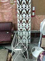 Overall view of three fence panels leaning behind white wire grid plant stand and cast iron flower pot
