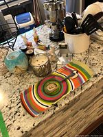 Overview of lot items on marble kitchen counter including spice rack, utensils holder, linens, ceramic vase, candles, and decorative figurines.
