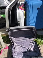 Three hard shelled suitcases, one open showing fabric lined interior spaces. Blue and two white suitcases grouped together.