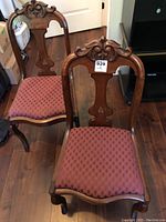 Photo shows two occasional chairs with wooden carved backs and upholstered seats in mauve fabric.