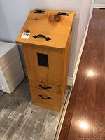 Full view of the tall wooden storage bin with slanted lid, metal handles, and drawers