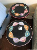 Two round folding side tables viewed from above, showing the colorful decorative design on the black tops.