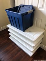 Four white plastic under-bed storage bins stacked with a blue plastic bin on top, all with lids.