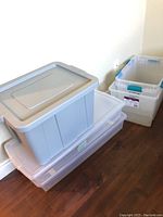 Stacked plastic bins. Three bins stacked, two with gray lids, one gray bin on top, two clear bins with blue latches beside stack.