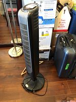 Full view of black Bionaire tower floor fan standing on circular base with power cord coiled at base.