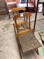Two folding chairs made of wood with upholstered seats, showing aged wear and fabric fraying on one seat.