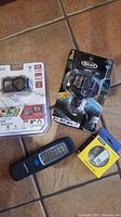 Bike LED cycling hub light in black with mounting bracket, black handheld LED flashlight, and yellow headlamp in retail packaging on tiled floor.