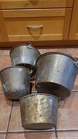 Overview of four brass metal planter pots with four handles each, showing wear and patina on surfaces.
