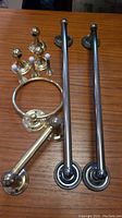 Photo showing two chrome towel rods, brass towel ring, two brass door stoppers, and two brass towel hangers on a wooden surface.