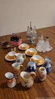 Overview of all miniatures including Coke bottles, porcelain pitchers, teacups, saucers, and crystal cruet set on wooden table